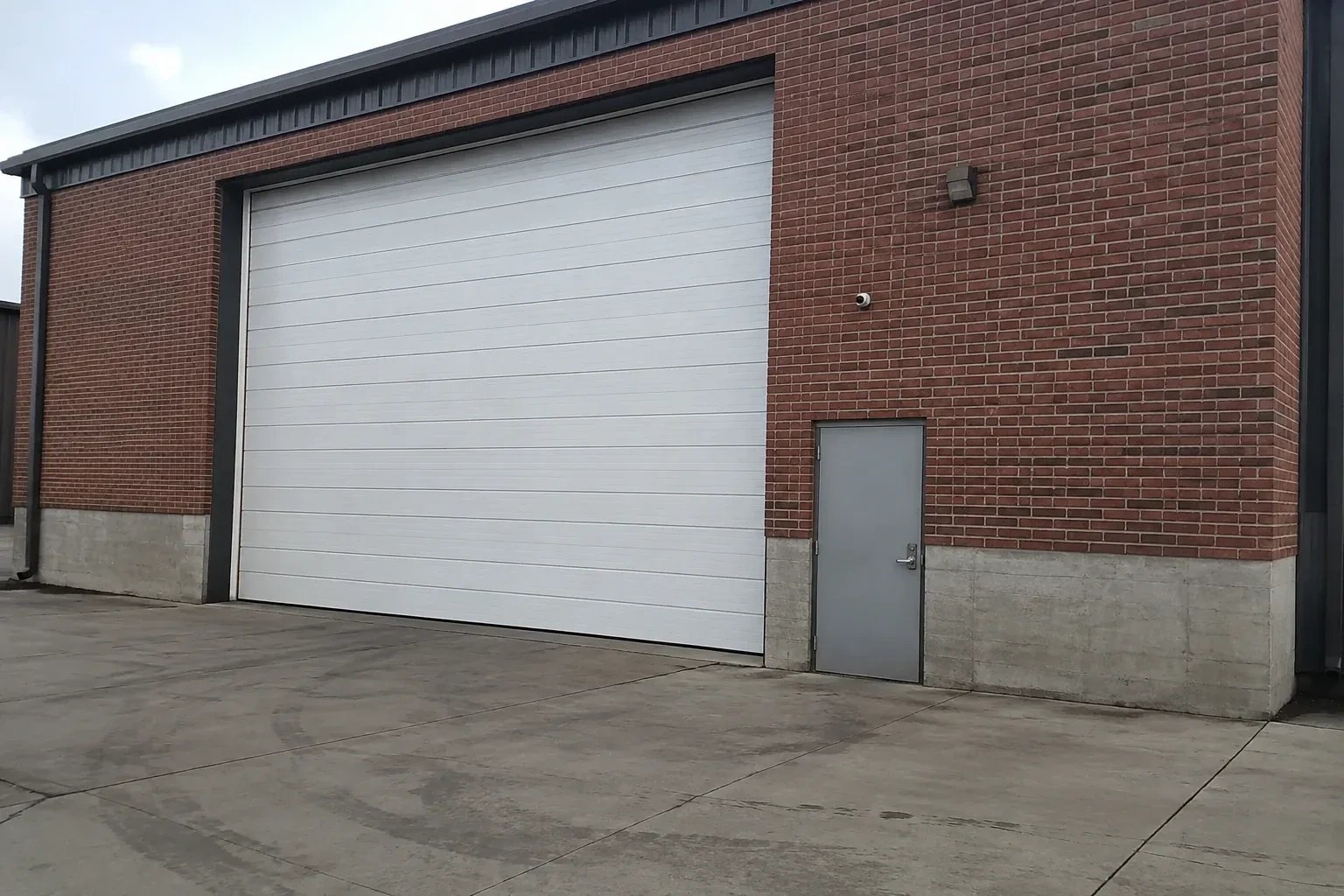 Tall closed sectional loading door beside a personnel door at a brick unit. — Commercial Sectional Door Repair, Brampton